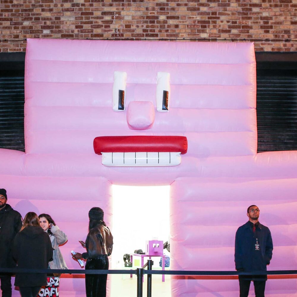 People standing before giant inflatable pink wall with face
